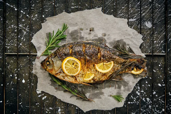 Fırında limon ve parşömen kağıdında biberiye ile pişirilmiş balık, ızgara üzerine serilmiş koyu arkaplan.