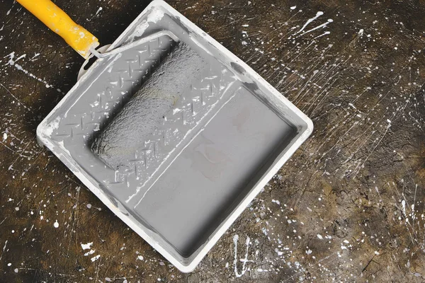 Tablada sarı saplı boya silindiri var. Beton zeminde gri boya var.