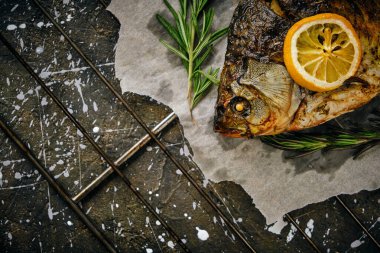 Fırında limon ve parşömen kağıdında biberiye ile pişirilmiş balık, ızgara üzerine serilmiş koyu arkaplan.