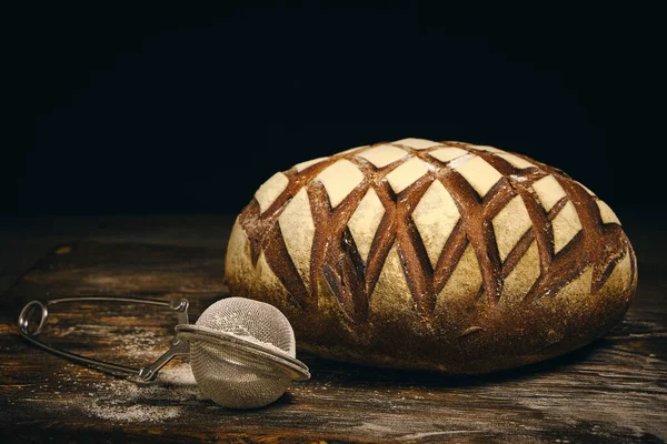 Üzerine un serpiştirilmiş çavdar ekmeği ve koyu arkaplana serpiştirmek için elek.