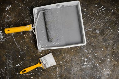 Boya silindiri, sarı saplı fırça tepside beton zeminde gri boyalı silindir için.