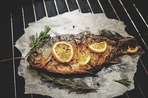 Fırında limon ve parşömen kağıdında biberiye ile pişirilmiş balık, ızgara üzerine serilmiş koyu arkaplan.