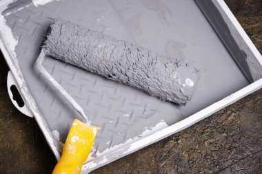 Tablada sarı saplı boya silindiri var. Beton zeminde gri boya var.