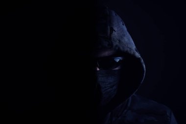 Stylish man in dark hoodie with black glasses and mask dark background, hacker, attacker and bandit