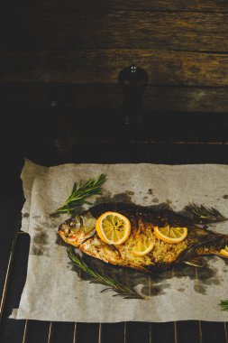 Ot ve limonlu fırınlanmış balık parşömen kağıdına konur ve arka planda pipetler bulunur.