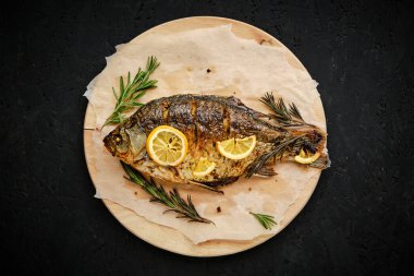 Limonlu ve biberiyeli fırında pişirilmiş balık kesme tahtası ve parşömen kağıdı. Koyu arkaplanda.