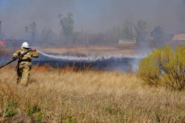 Firefighter extinguishes burning, dry grass from fire hose