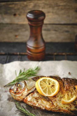 Ot ve limonlu fırınlanmış balık parşömen kağıdına konur ve arka planda pipetler bulunur.