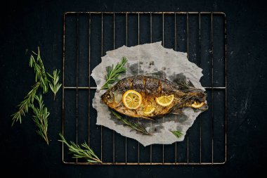 Fırında limon ve parşömen kağıdında biberiye ile pişirilmiş balık, ızgara üzerine serilmiş koyu arkaplan.