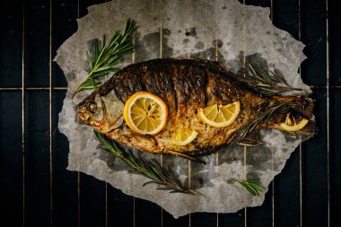 Fırında limon ve parşömen kağıdında biberiye ile pişirilmiş balık, ızgara üzerine serilmiş koyu arkaplan.