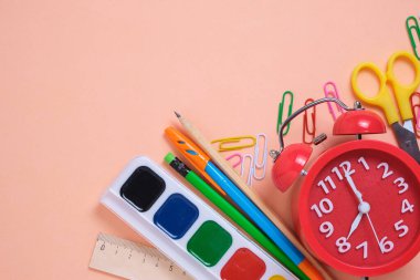 Kırmızı alarm saati, okul malzemeleri ve pembe arka planda kırtasiye malzemeleri.