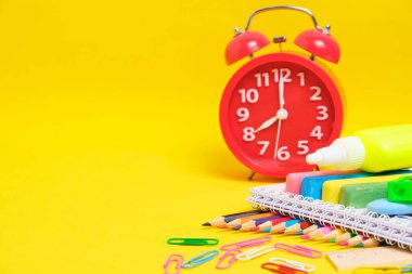 Kırmızı alarm saati ve okul malzemeleri sarı arka plan. Çocuğu okula hazırlıyorum.