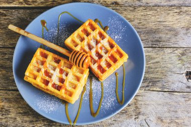Tatlı waffle 'lar, üzerine bal serpilmiş ve üzerine pudra şekeri serpiştirilmiş mavi tabakta.