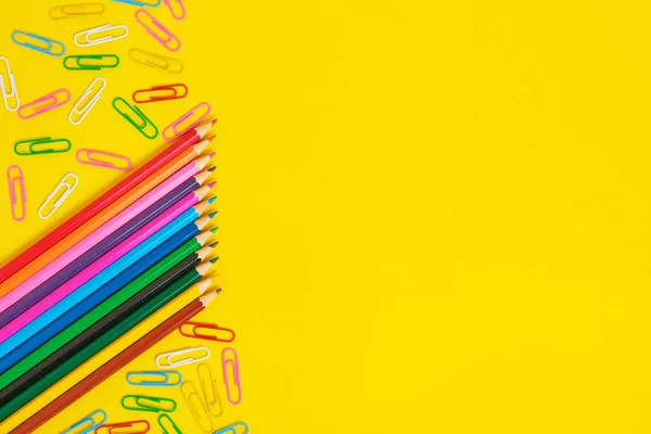 Colored pencils and paper clips yellow background