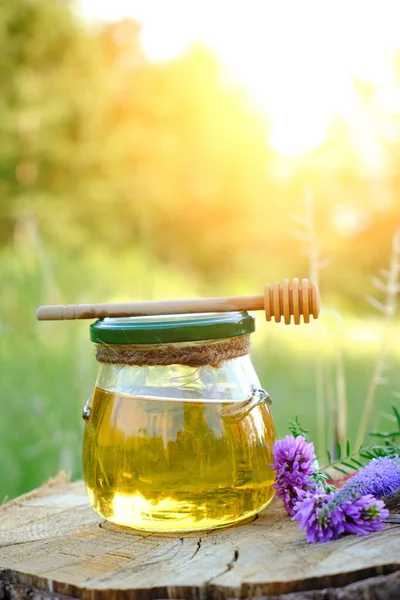 Jar honey and spoon for honey in forest on stump with meadow flowers