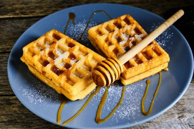 Tatlı waffle 'lar, üzerine bal serpilmiş ve üzerine pudra şekeri serpiştirilmiş mavi tabakta.
