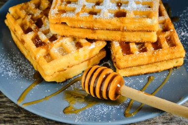 Tatlı waffle 'lar, üzerine bal serpilmiş ve üzerine pudra şekeri serpiştirilmiş mavi tabakta.