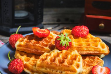 Çilekli waffle ve bal, tabakta tatlı hamur işleri, arka planda kahve öğütücüsü ve mumlu dekoratif lamba.