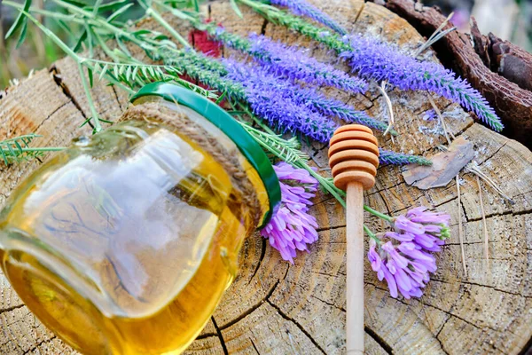 Jar honey and spoon for honey in forest on stump with meadow flowers