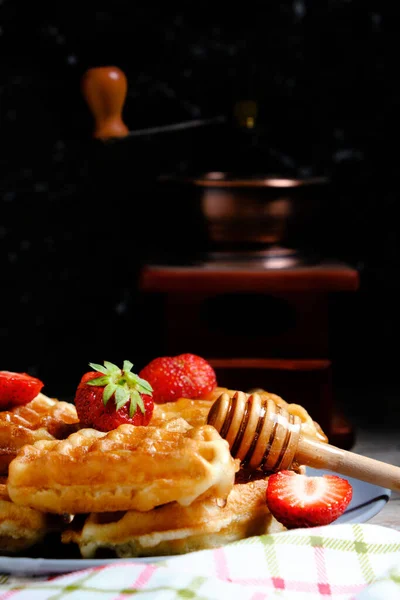 Waffles with strawberries and honey, sweet pastries on plate, against background coffee grinder