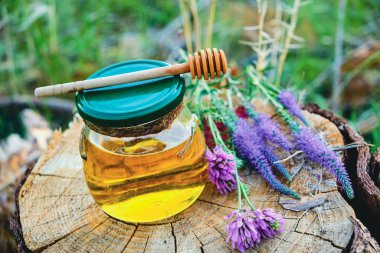 Kavanozda bal ve kaşık ormanda çayırda çiçeklerle birlikte.