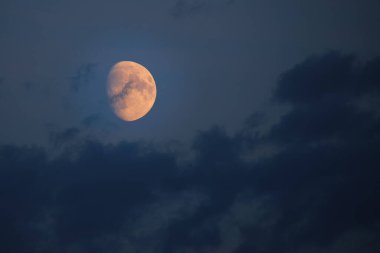 Bright orange moon against dark sky and clouds
