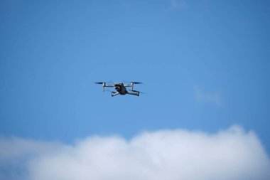 Quadrocopter flying against background blue sky and clouds