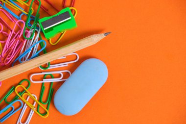 Stationery for schoolchildren paper clips, pencil, eraser and sharpener on an orange background