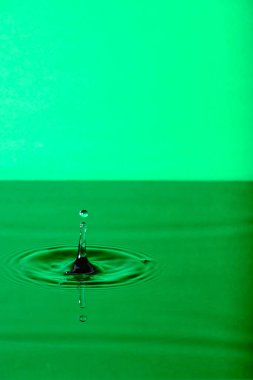 Splash drop of water with diverging water circles, on green background