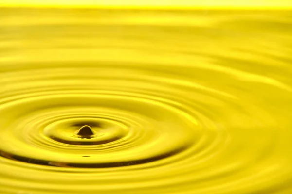 Splash drop of water with diverging water circles, on yellow background