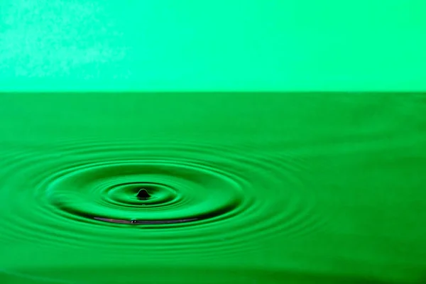 Splash drop of water with diverging water circles, on green background