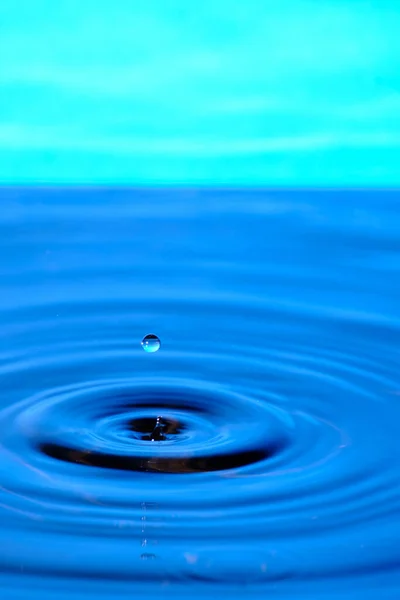 Splash drop of water with diverging water circles, on blue background