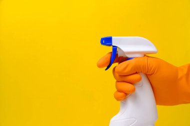 Pencereleri temizlemek ve sarı arka planda eldivenle su tesisatı yapmak için sprey sıkın
