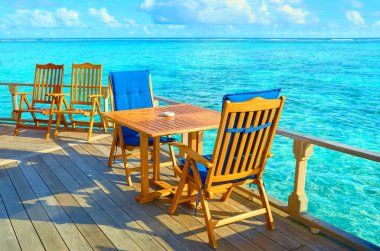 Gök mavisi okyanusun kıyısında sandalyeli masalar. Maldivler 'de tatiller.