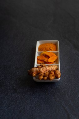 Üç sunumda zerdeçal, kök, lamine ve toz beyaz bir tabakta ve siyah bir arkaplanda.