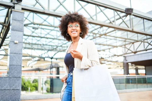 Happy afro woman shopping in a mall. She is holding her bags while walking. Curly afro style hair.