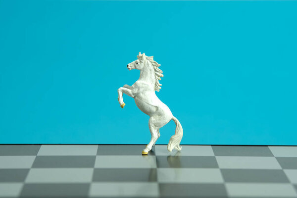 Miniature of white prancing horse standing on chessboard isolated on blue background. Image photo