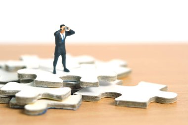 İşadamları yapboz parçalarının üzerinde tahta masanın üstünde dürbünle duruyorlar. Minyatür minyatür insanlar, oyuncaklar fotoğrafçılık..