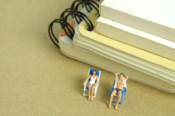 Miniature people toy figure photography. Office work break concept, Men and girl relaxing at beach chair in front of book document. image photo