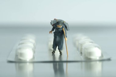 Minyatür insanlar oyuncak fotoğrafçılık. İlaç haplarının ortasında değnek ya da değnekle yürüyen yaşlı bir adam. Tıbbi erişim konsepti. Resim fotoğrafı.