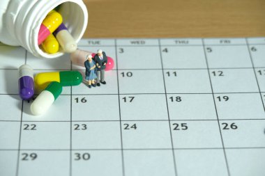 Minyatür insanlar kavramsal fotoğrafçılık oyuncakları. İlaç hapı ve şişeyle takvimin üstünde duran yaşlı bir çift. İlaç rutini konsepti. Resim fotoğrafı.