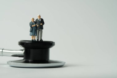 Minyatür insanlar kavramsal fotoğrafçılık oyuncakları. Steteskopun üstünde duran yaşlı bir çift sağlık kontrolü yapıyor. Beyaz arka planda izole edilmiş. Resim fotoğrafı.