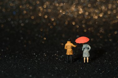 Minyatür insanlar oyuncak fotoğrafçılık. Yağmurlu günlerde şemsiye kullanan bir çift. Güzel, altın sarısı, Bokeh şehrinin aydınlık arka planı. Resim fotoğrafı.