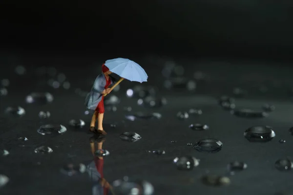 Miniature people toy figure photography. A woman wearing a raincoat using umbrella, walking on the street during a storm, against a very strong wind. Dark cloudy, thunderstorm background. Image photo