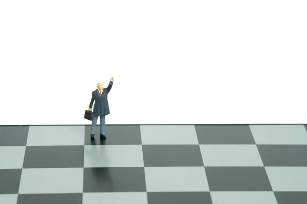 Miniature people toy figure photography. Voice your strategy concept. A businessman standing above chessboard while raise his hand. Isolated on white background. Image photo
