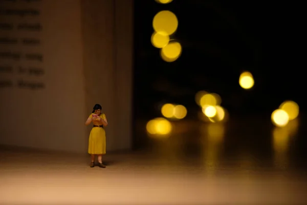 Miniature people toy figure photography. A girl reading a book at night with bokeh defocused light lamp, bed time routine before sleep. Image photo