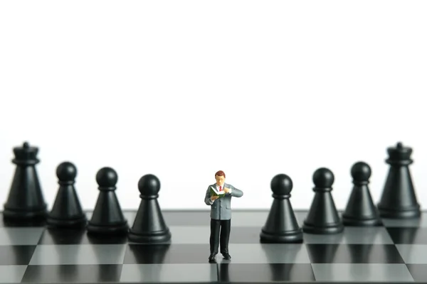 Miniature people toy figure photography. A men student standing above chessboard with pawn and knight, isolated on white background. Image photo