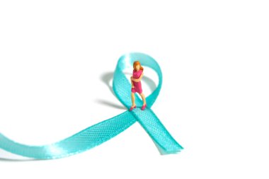 Miniature people figure toys photography. Ovarian and breast cancer awareness day concept. Girl, teenage, woman standing above green turquoise teal ribbon. Image photo