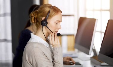 Kafkasyalı dost canlısı iş kadını güneşli ofiste kulaklıkla konuşuyor. Çağrı merkezi ve çeşitli iş grupları