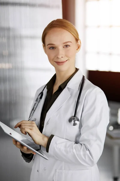 Amichevole medico femminile sorridente utilizzando tablet computer in clinica soleggiata. Una dottoressa al lavoro. Servizio medico perfetto in ospedale. Concetto di medicina — Foto Stock